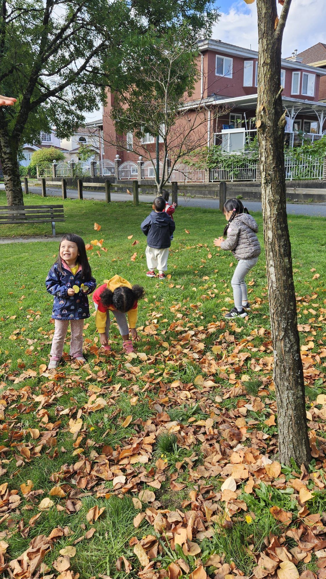 Daycare - Kids playing at park. Picking up fall leaves on the ground